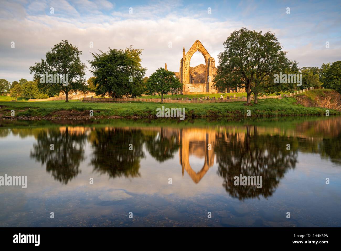 Bolton Abbey catches the first direct light of a beautiful summer morning, with the old ruin reflected in the slow flowing River Wharfe beneath. Stock Photo