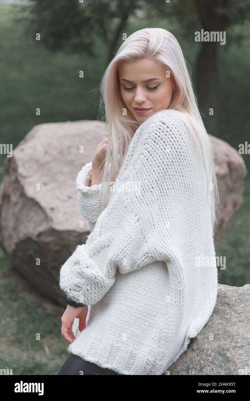 Young blonde female wearing knitted white sweater. Women fashion concept. Stock Photo