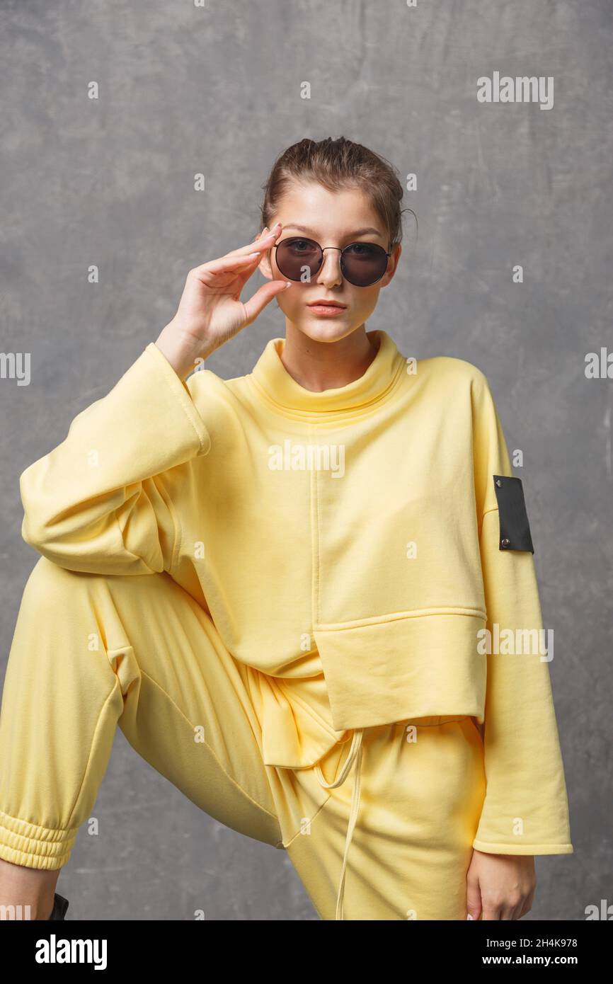 Young woman in yellow sweatshirt and sunglasses on a gray background. Stock Photo