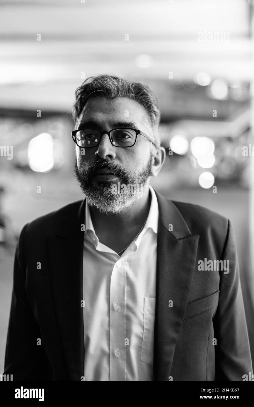 Black and white portrait of handsome Indian businessman in city at night thinking Stock Photo