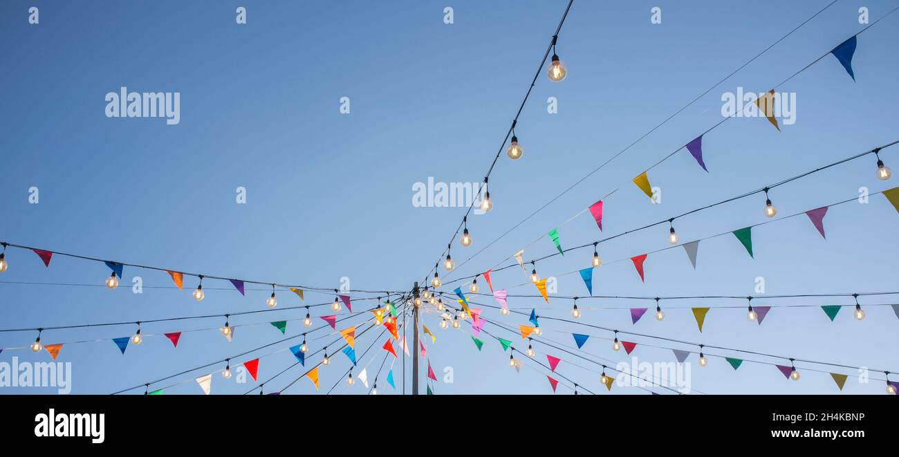 Garland with colorful pennants and light bulbs on pole over blue sky. Long format. Stock Photo