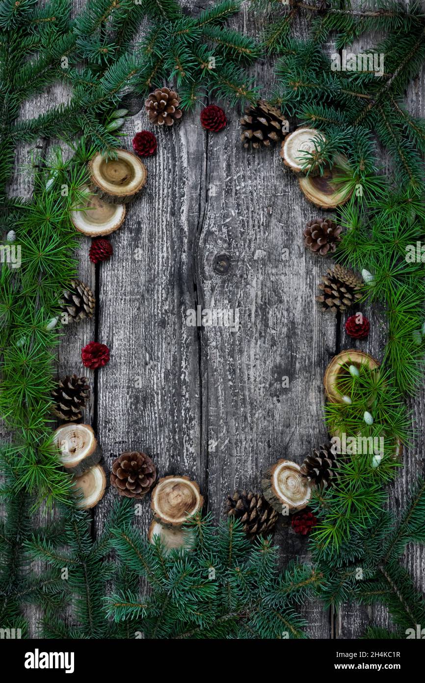 Christmas tree branches ,pine cones and wood logs on rustic wooden background with empty space in the middle. Flat lay, copy space, top view. Stock Photo