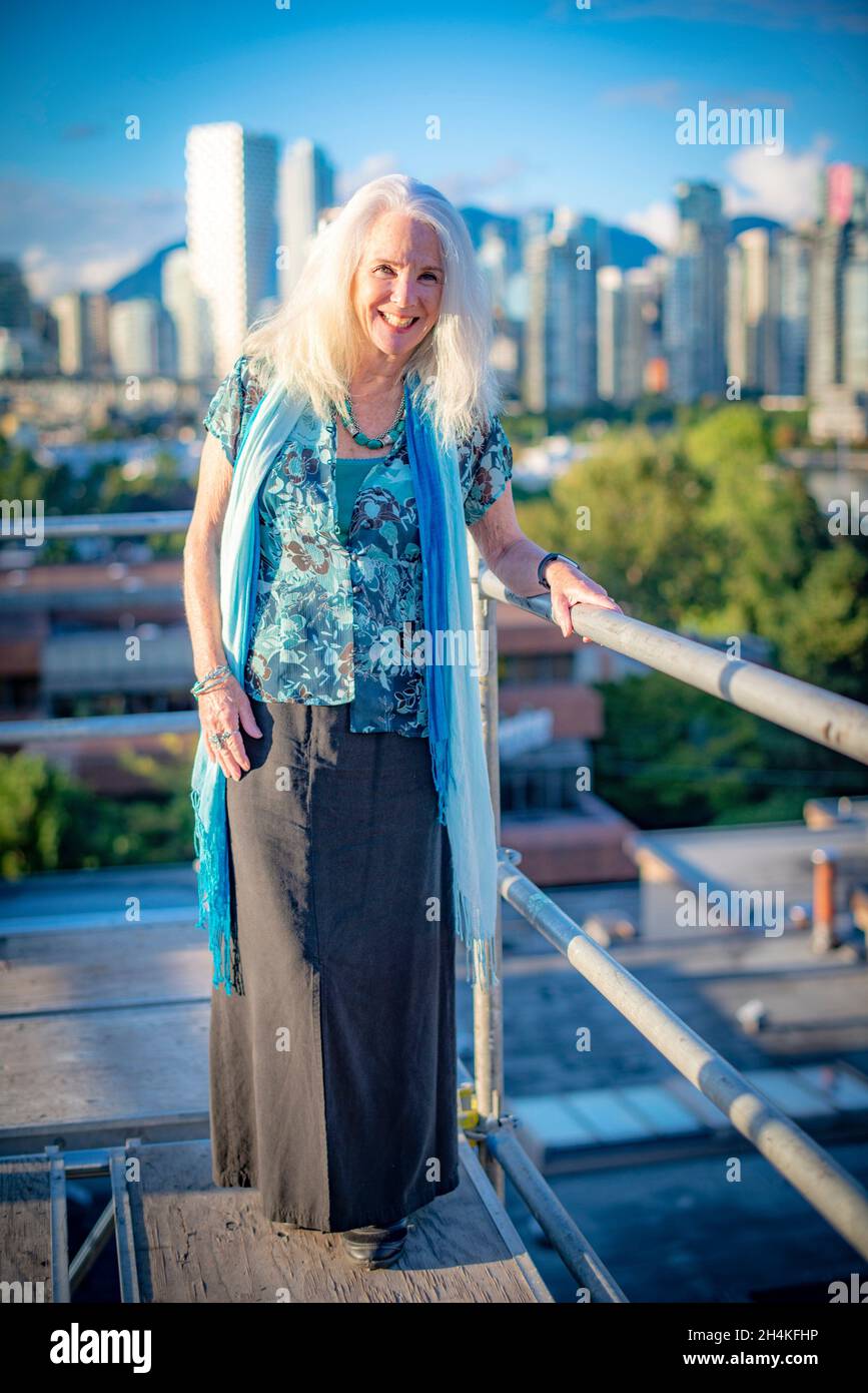 A woman, 70, in a portrait on a scaffold overlooking downtown Vancouver, BC, Canada. Stock Photo