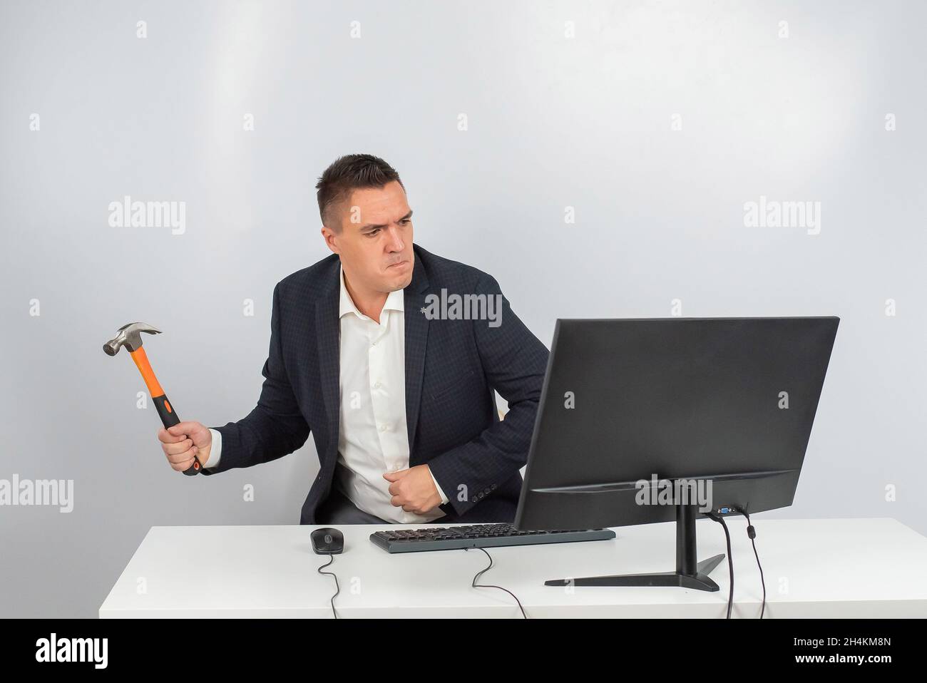 The man gets angry and smashes the monitor with a hammer. An office worker in a rage breaks the computer.  Stock Photo