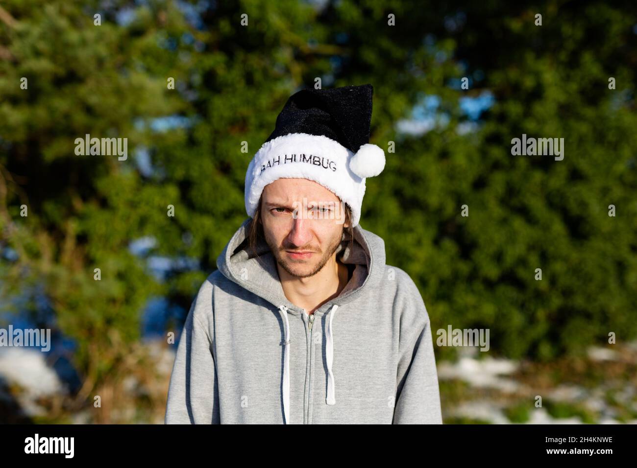 A grumpy young man wearing a black santa hat with the words Bah Humbug written on it Stock Photo