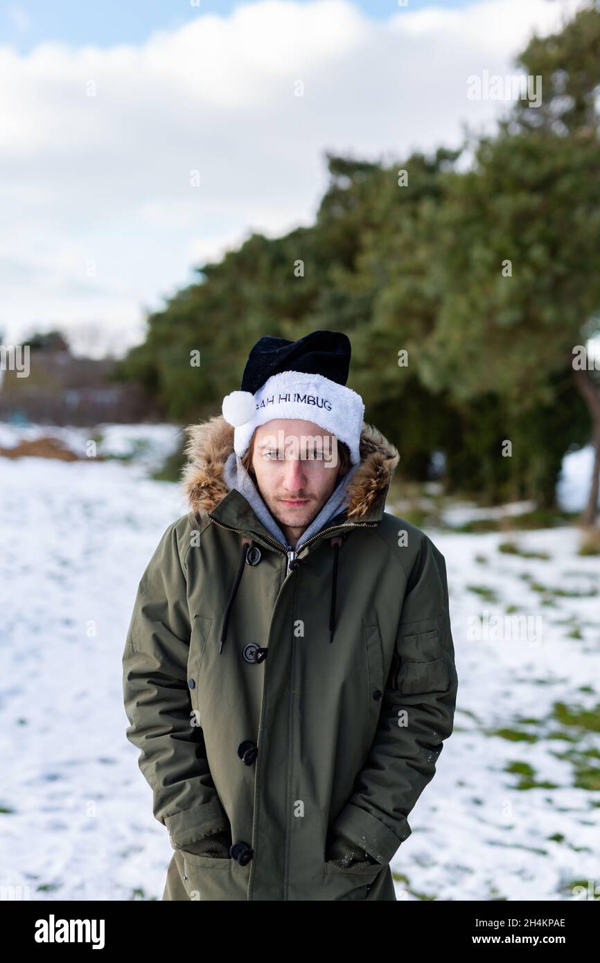A grumpy young man wearing a black santa hat with the words Bah Humbug written on it Stock Photo