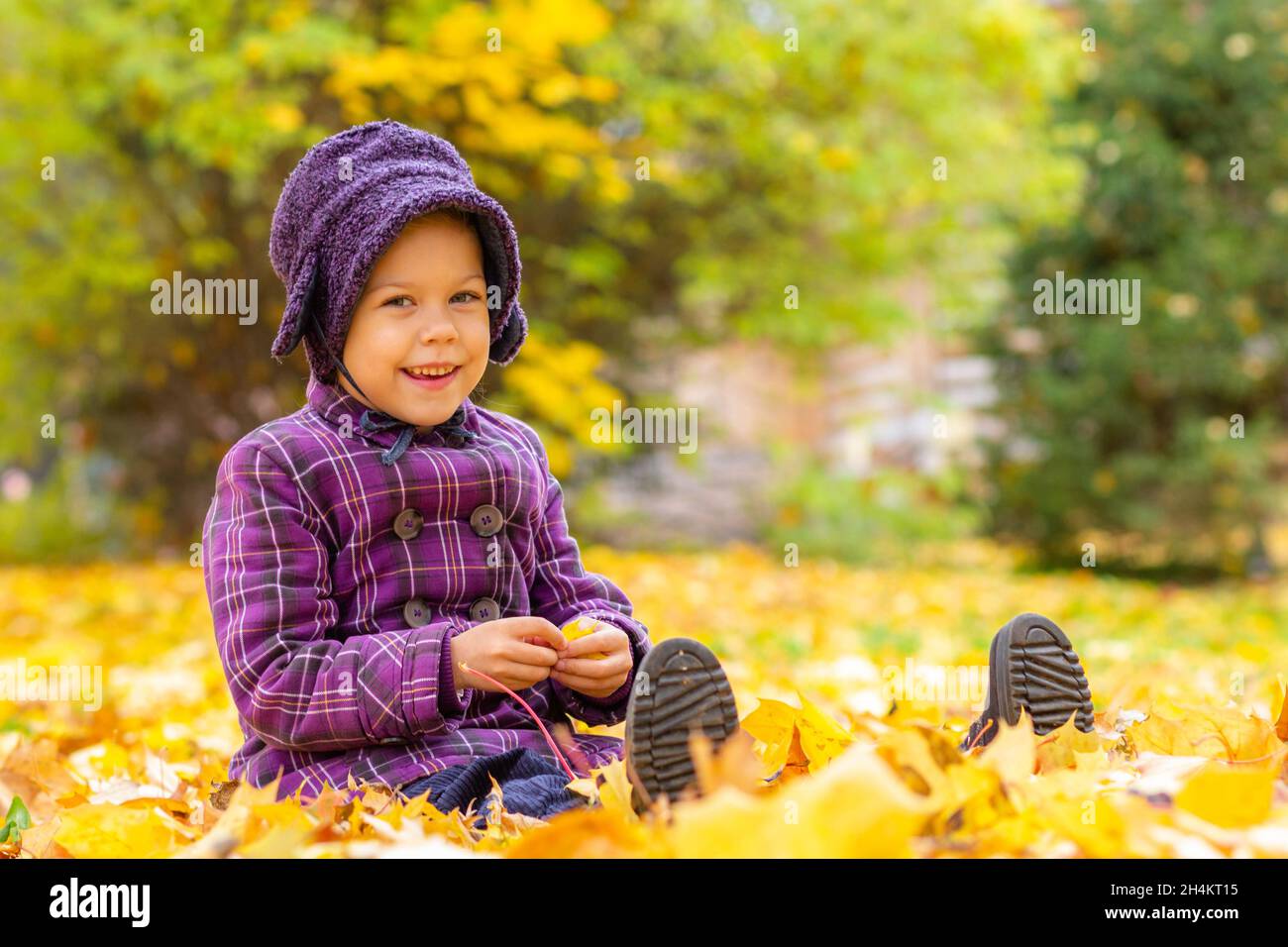 Caucasian little girl of five years old sitting on ground with yellow leaves in the autumn park Stock Photo
