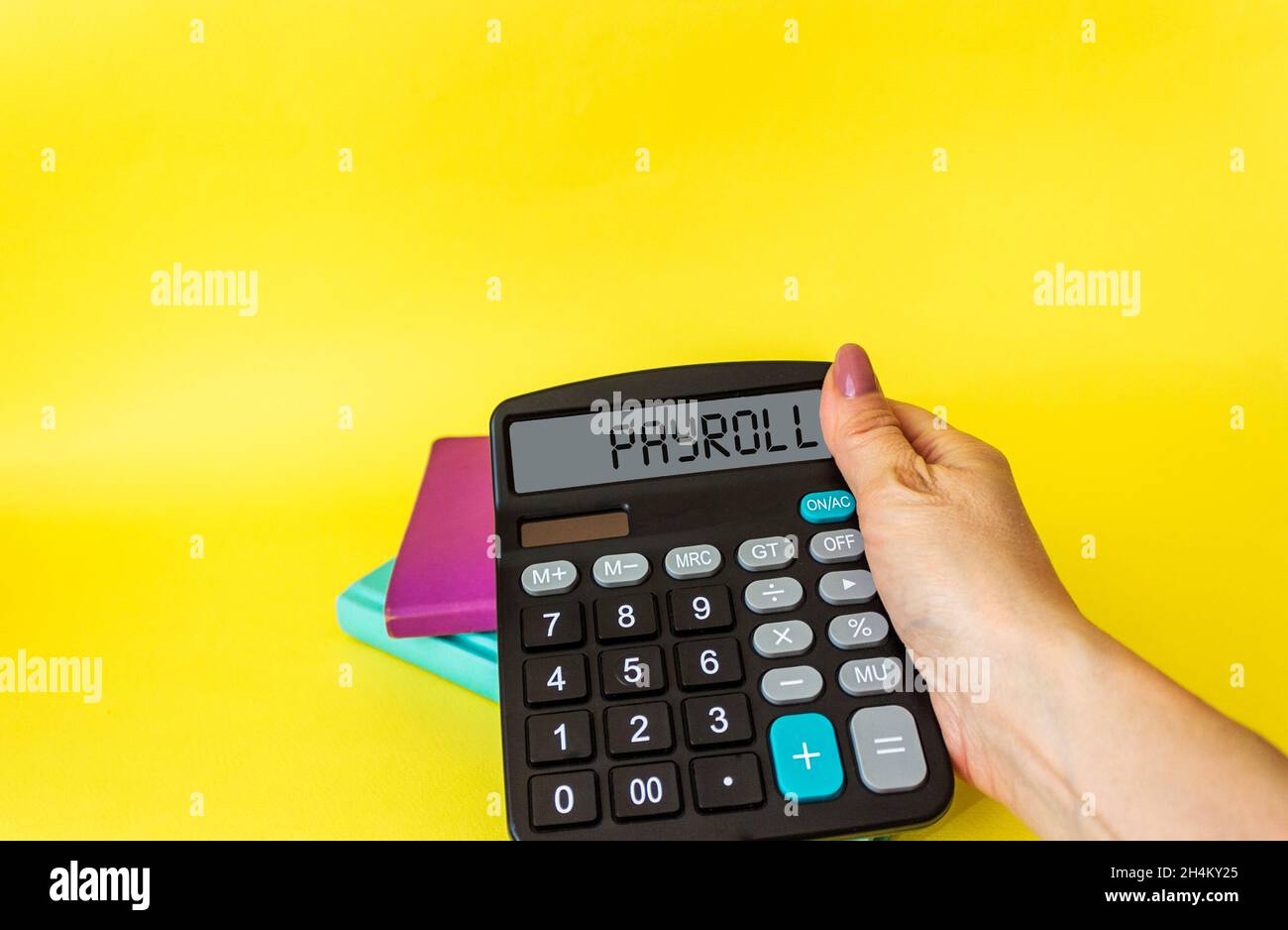 Female hand holds calculator with text on display PAYROLL, on yellow background Stock Photo