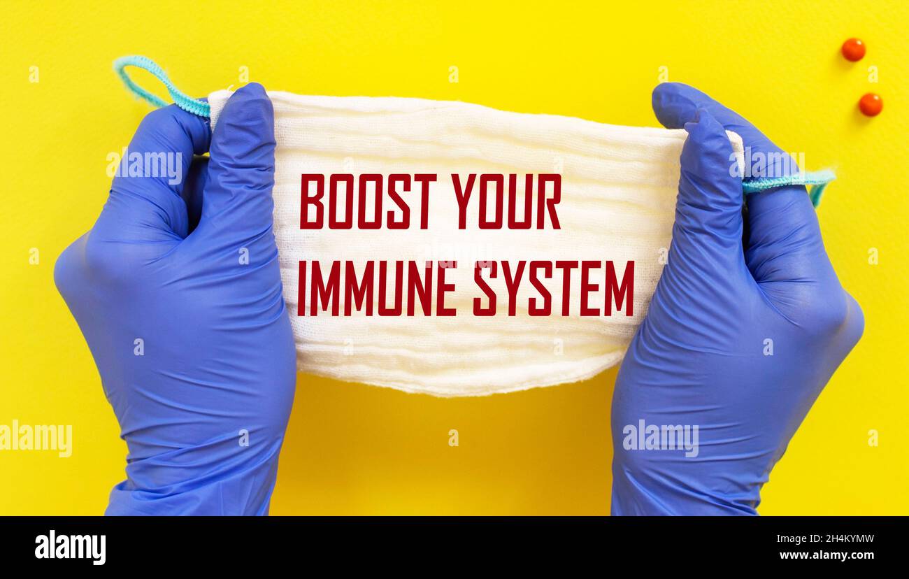 Boost your immune system. Woman in gloves holds a medical mask drawing attention to the phrase, close-up. Composition on yellow background Stock Photo