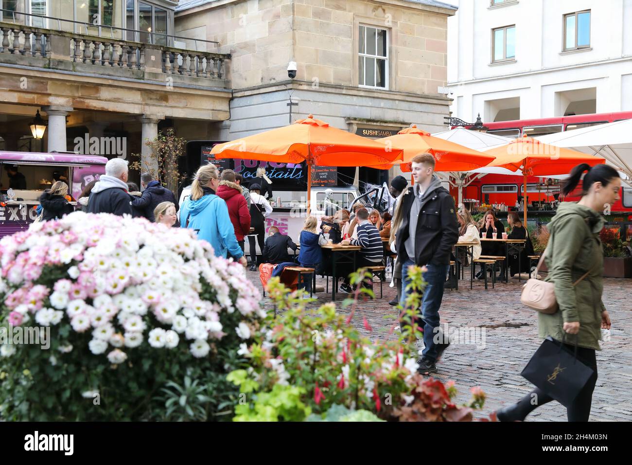 People relaxing in Covent Garden, by autumn flower displays, in London, UK Stock Photo