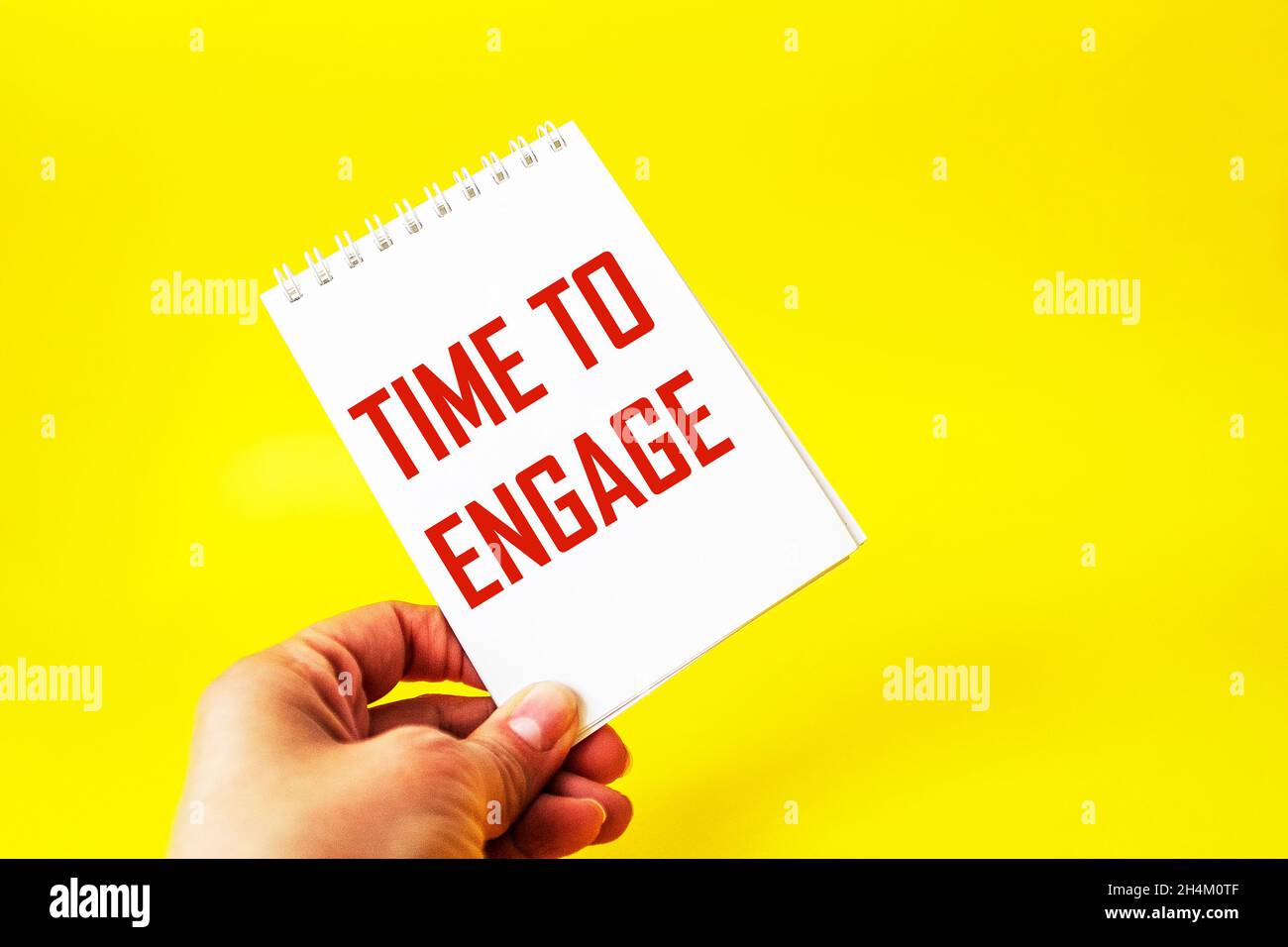 A female hand holds a card with the text TIME TO ENGAGE on a yellow background. Stock Photo