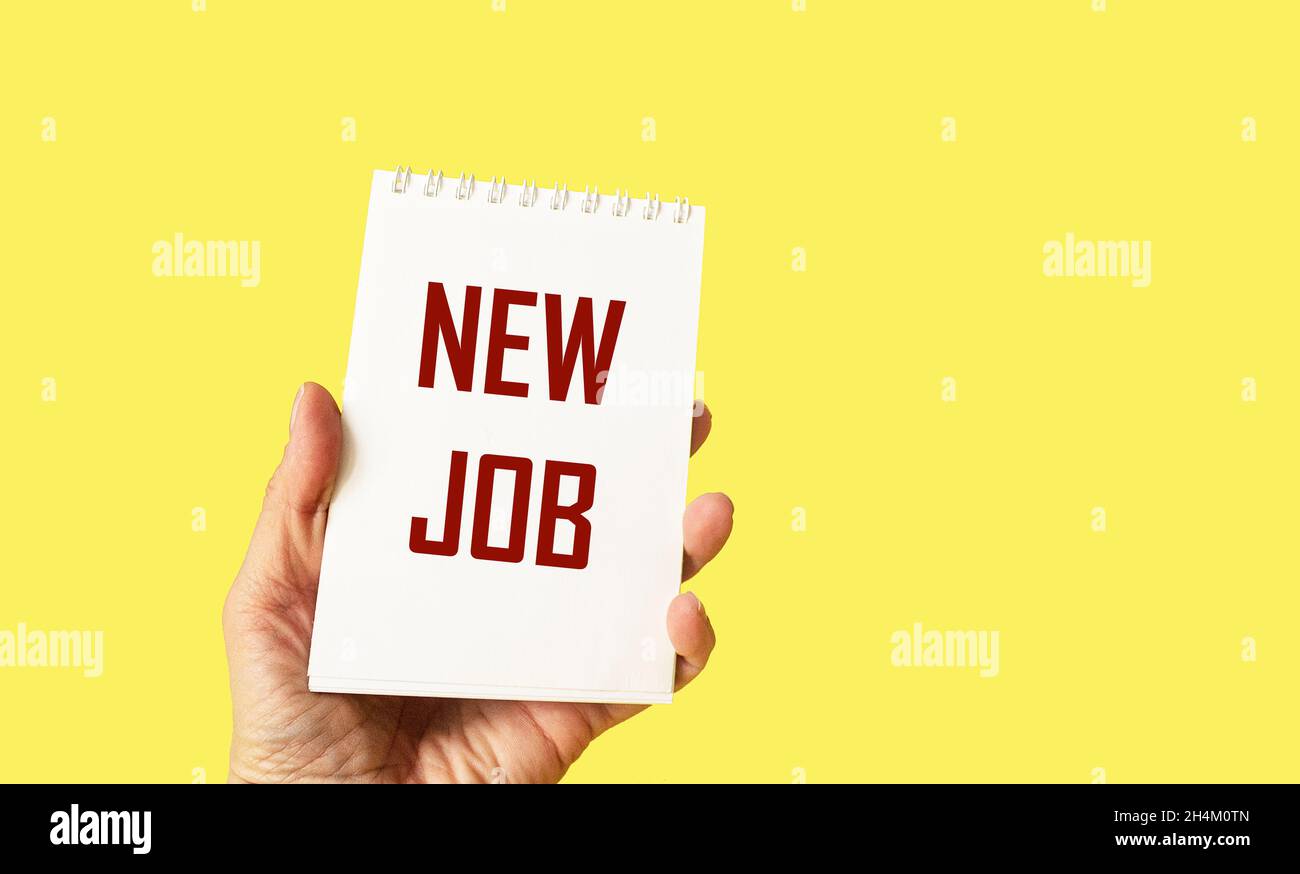 Hand holds notepad on yellow background with text NEW JOB Stock Photo
