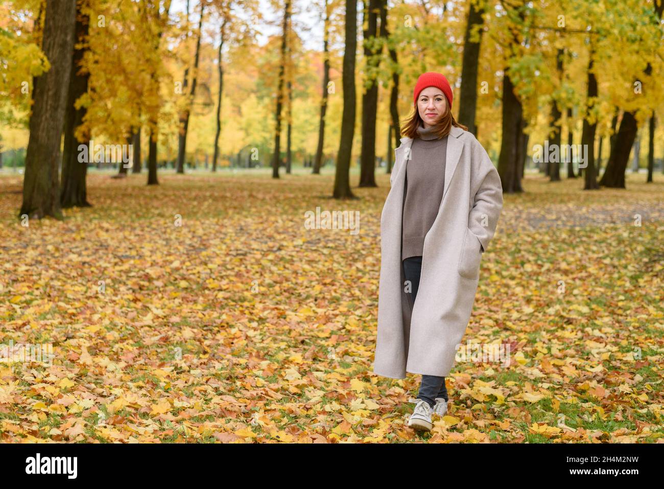 Portrait of walking woman in wool coat and red hat at autumn park Stock Photo