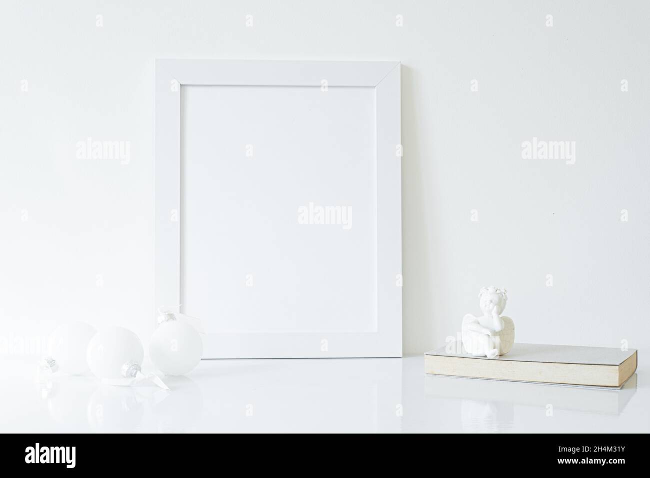 Mock up white frame with book, porcelain angel and white christmas decorations on shelf. Empty portrait frame against a white wall Stock Photo