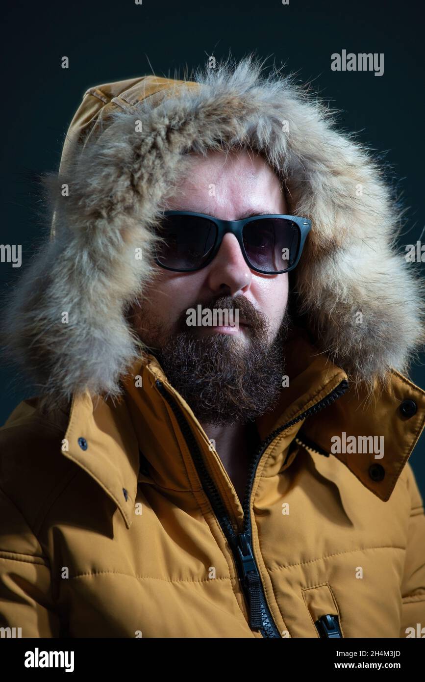 guy in a down jacket hood with fur, yellow jacket on a gray background. Stock Photo