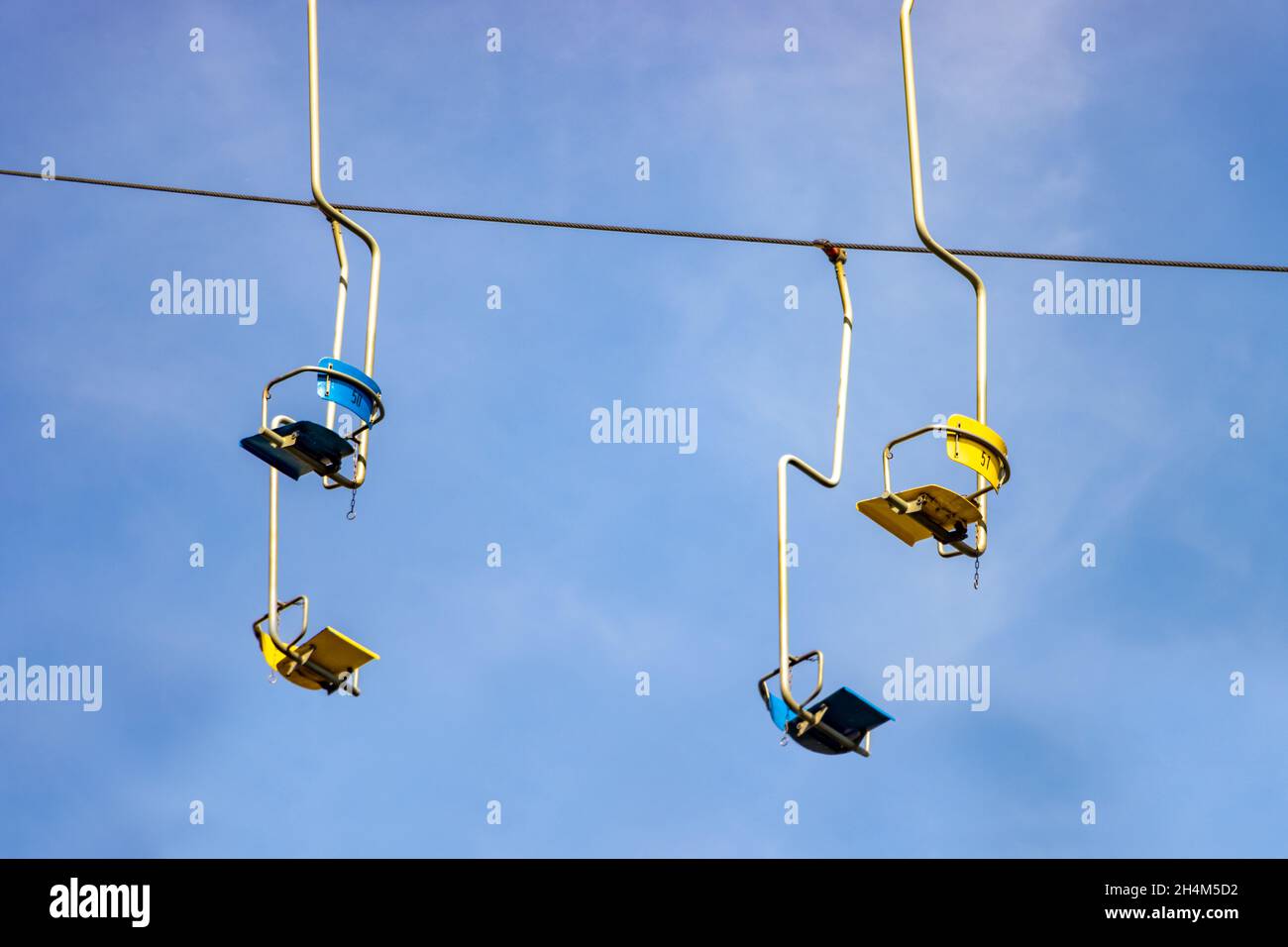 Empty chairlifts hanging on a cable on a background of blue sky Stock Photo