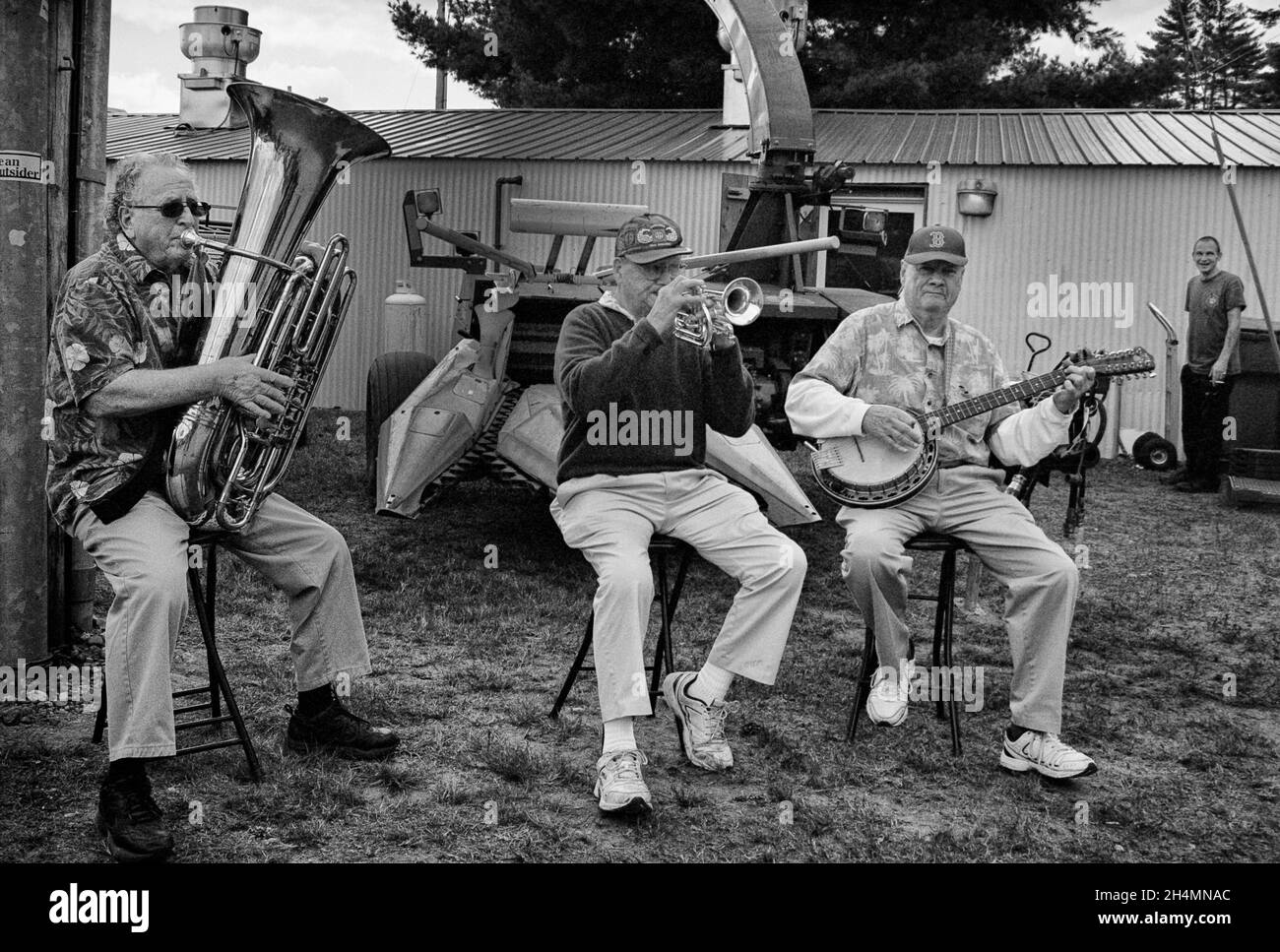 A trio of musicians play  on the side of the road while sitting on stools at the Deerfield Fair - Deerfield, New Hampshire. Black and White Ilford XP2 Stock Photo