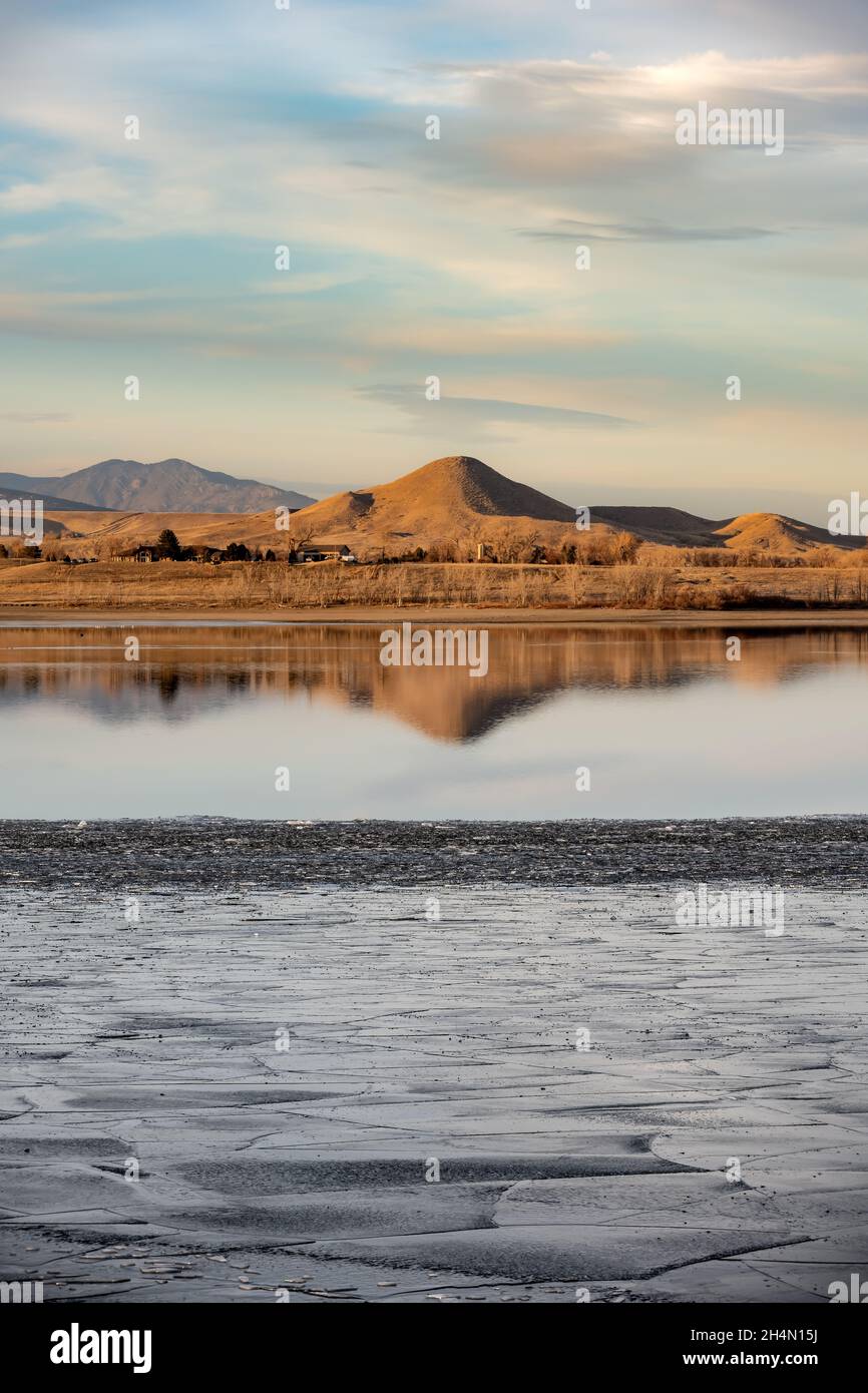 A hill is reflected in a partially frozen lake, Boulder Reservoir, with ice in the foreground Stock Photo