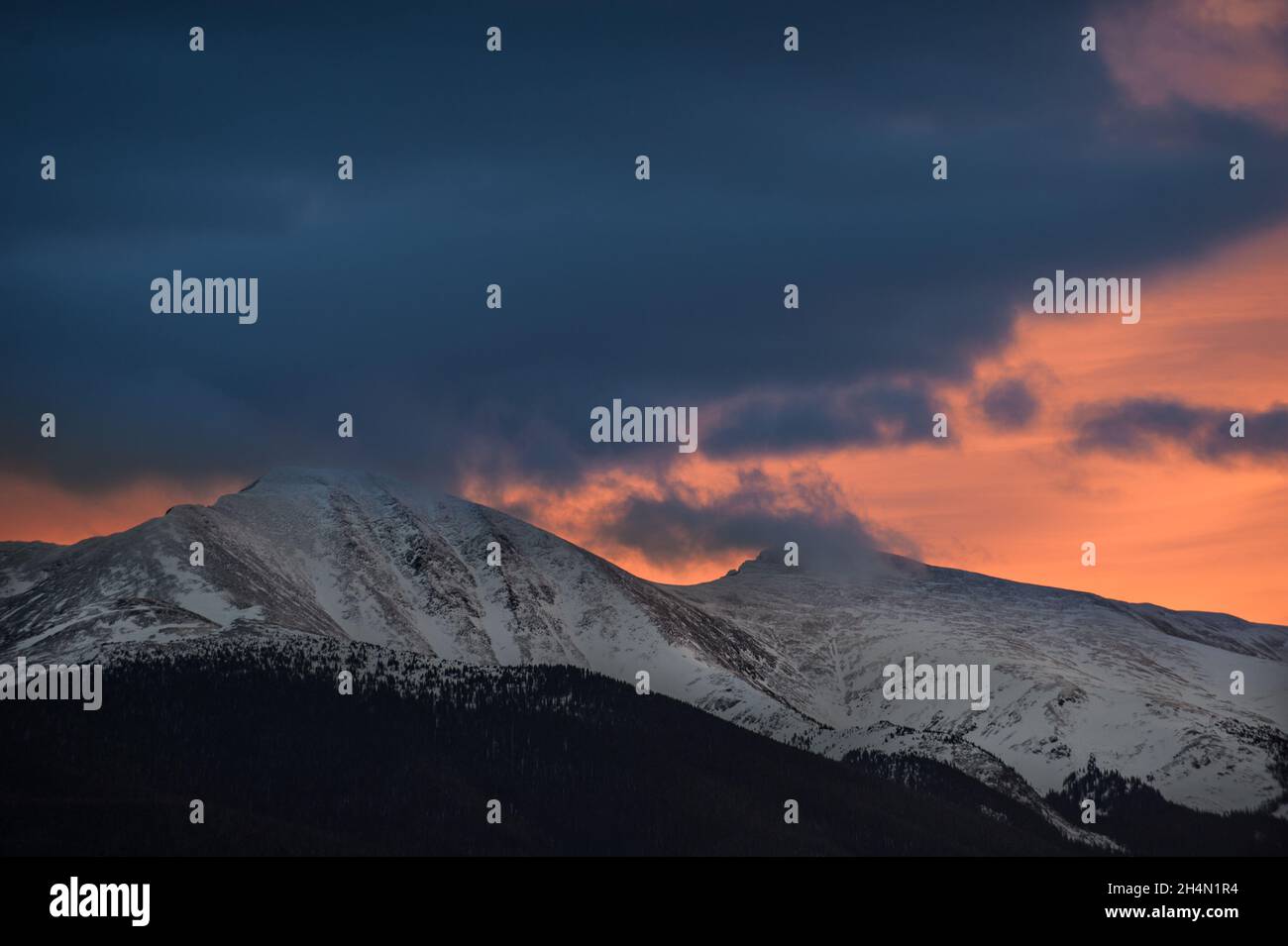 An orange sunset behind a snow covered mountain Stock Photo