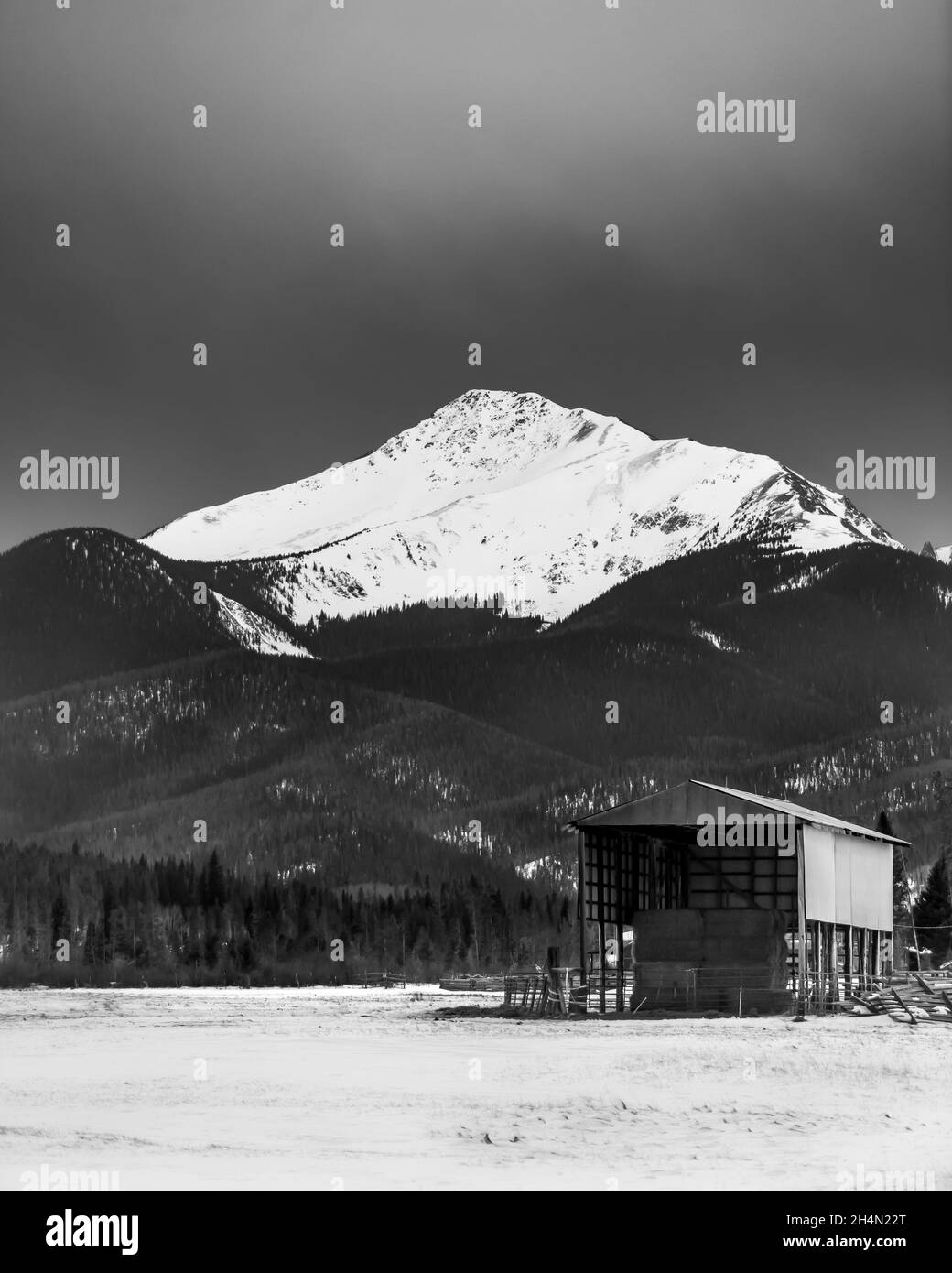 A snow capped peak (Byers Peak) towers above a hay barn of a ranch in the valley below Stock Photo