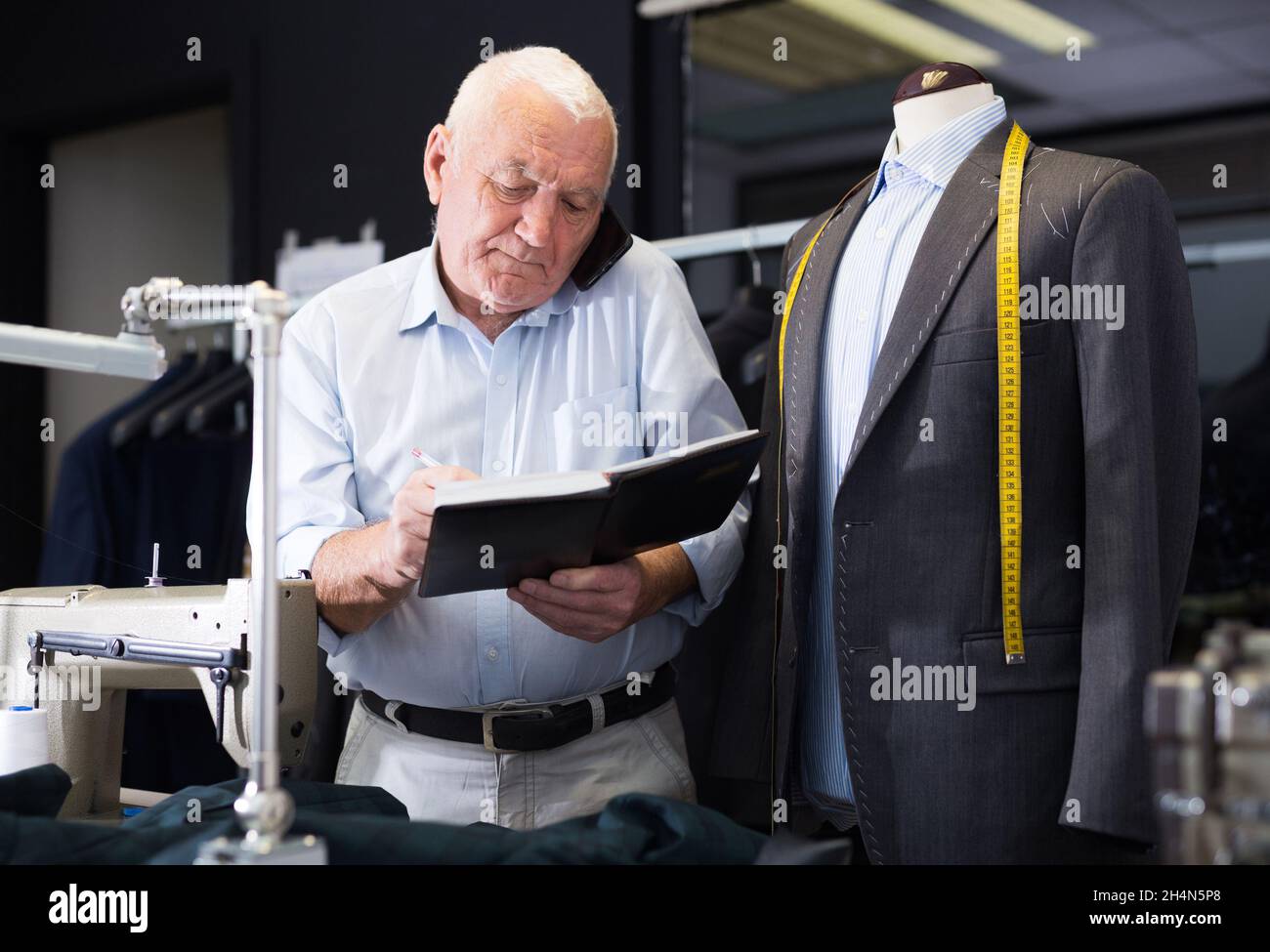 Professional tailor man talking on mobile phone and making notes in notebook Stock Photo