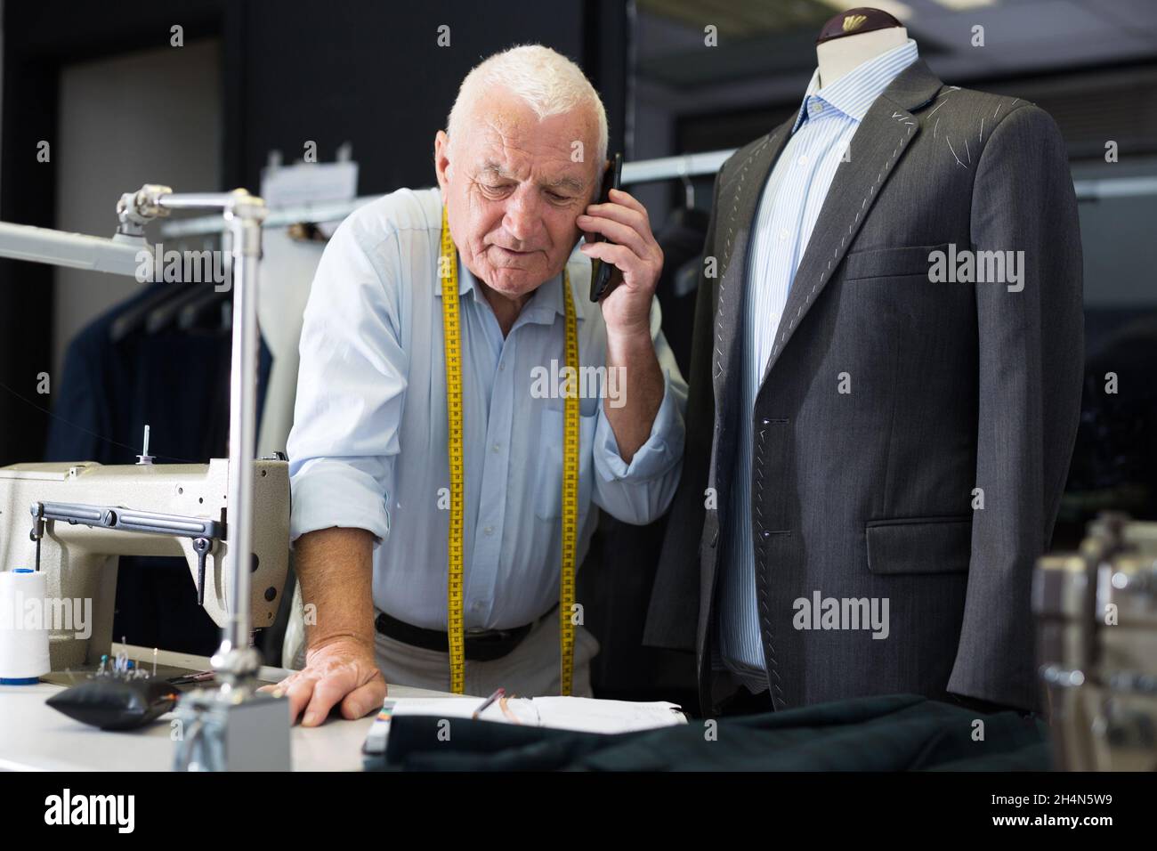 Professional tailor man talking on mobile phone and making notes in notebook Stock Photo