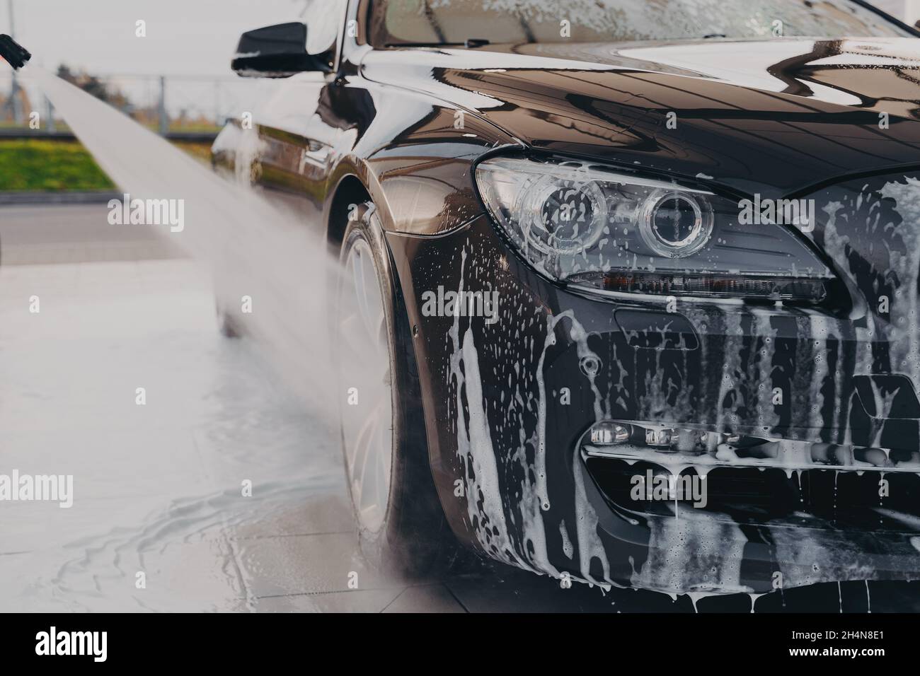 Professional car wash, spraying water from high pressure washer to rinse off suds Stock Photo