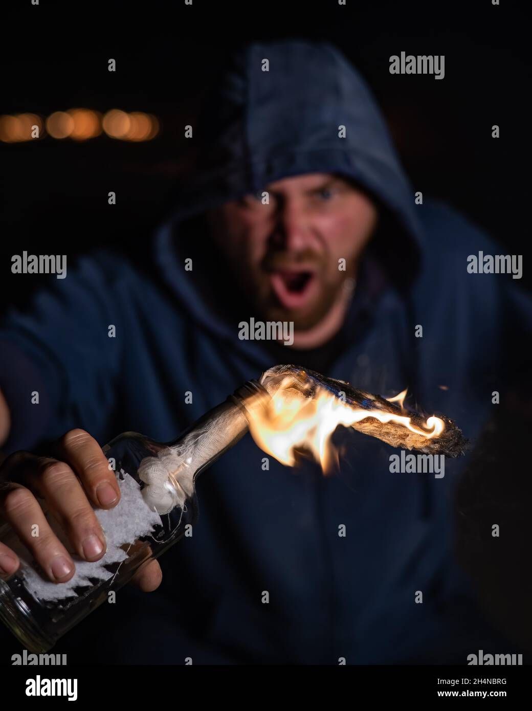 The man in the hood is holding a burning bottle. Molotov cocktail. Stock Photo