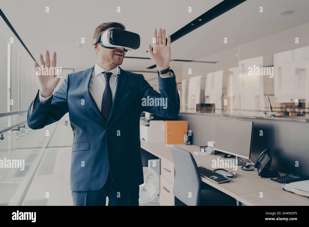 Businessman in virtual reality glasses standing near working desk in office Stock Photo