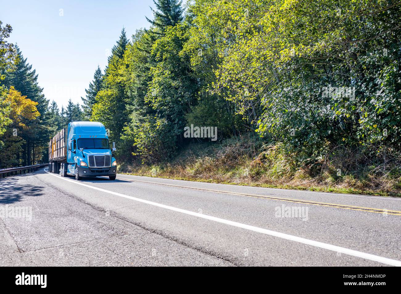 Powerful blue big rig classic semi truck transporting fruit harvest in fixed by slings wood boxes on flat bed semi trailer driving on the narrow windi Stock Photo