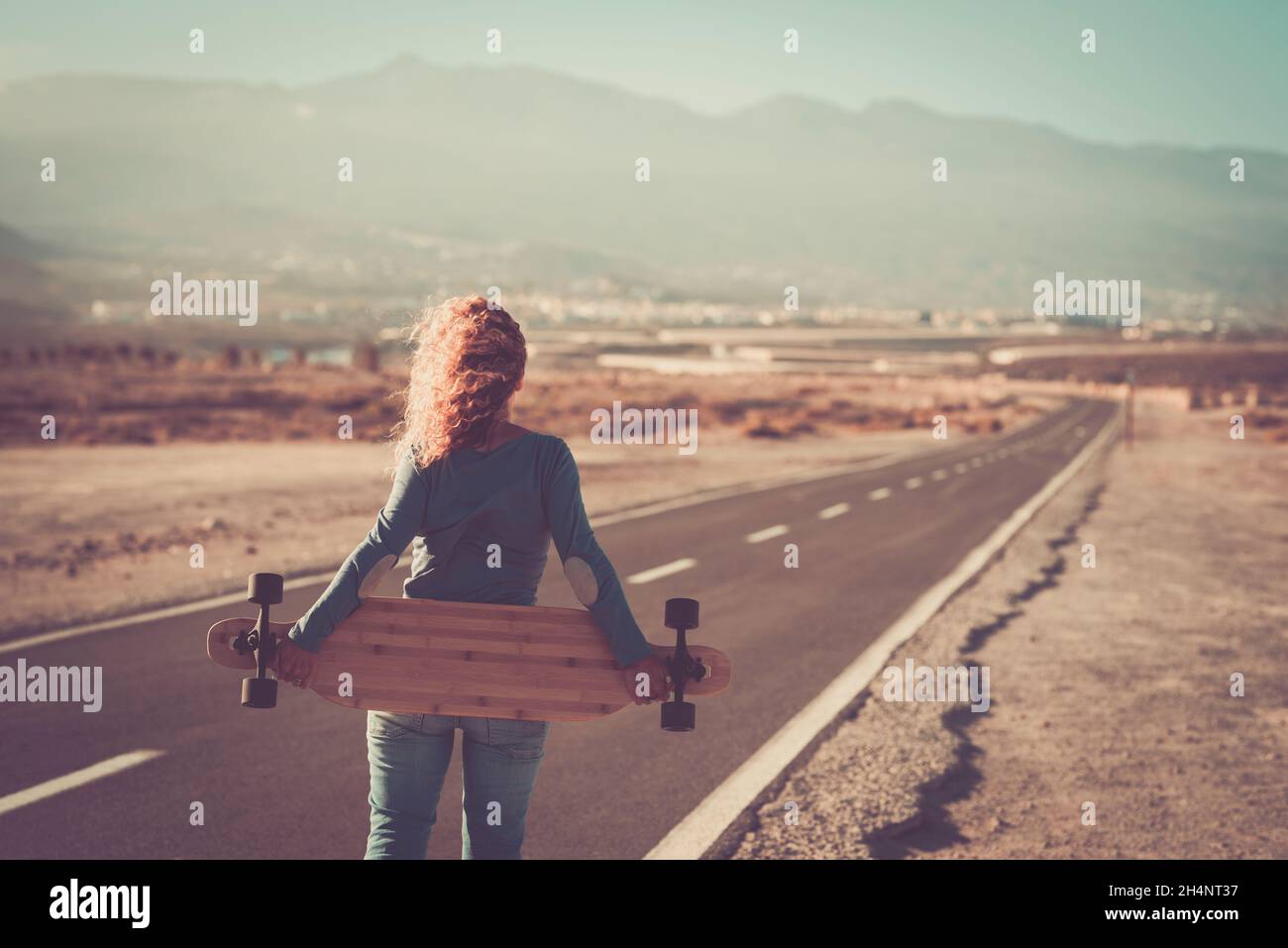 People travel and live freedom concept with standing woman walking on a straight road with long board. Back view. People and adventure destination lif Stock Photo