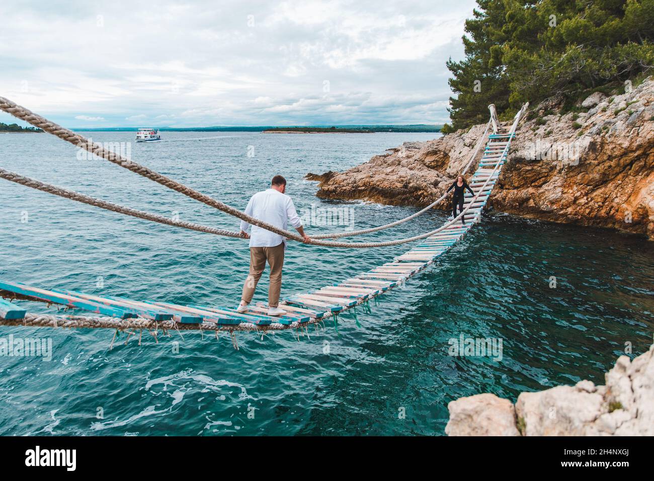 man walking by suspension bridge cross sea bay rocky cliff summer time ...