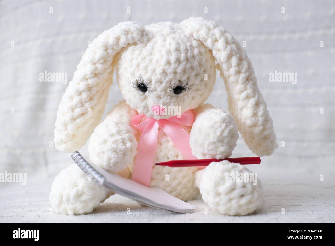 knit white rabbit sitting and writing a letter with red pebcil ...