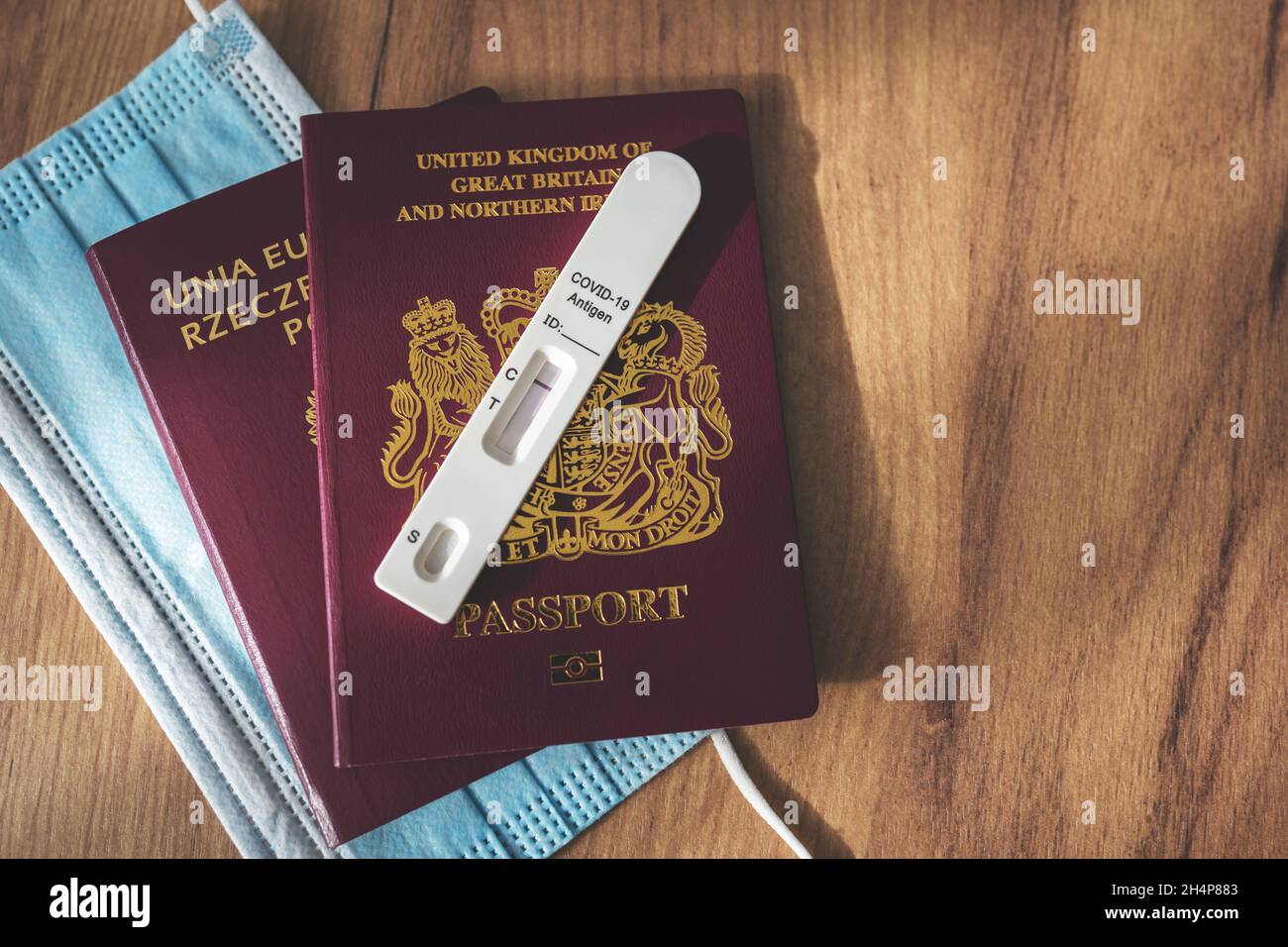 Negative rapid serology antigen COVID-19 test on red British and Polish passports and surgical face mask on wooden background. Travel during the coronavirus pandemic, avoid quarantine concept. Stock Photo