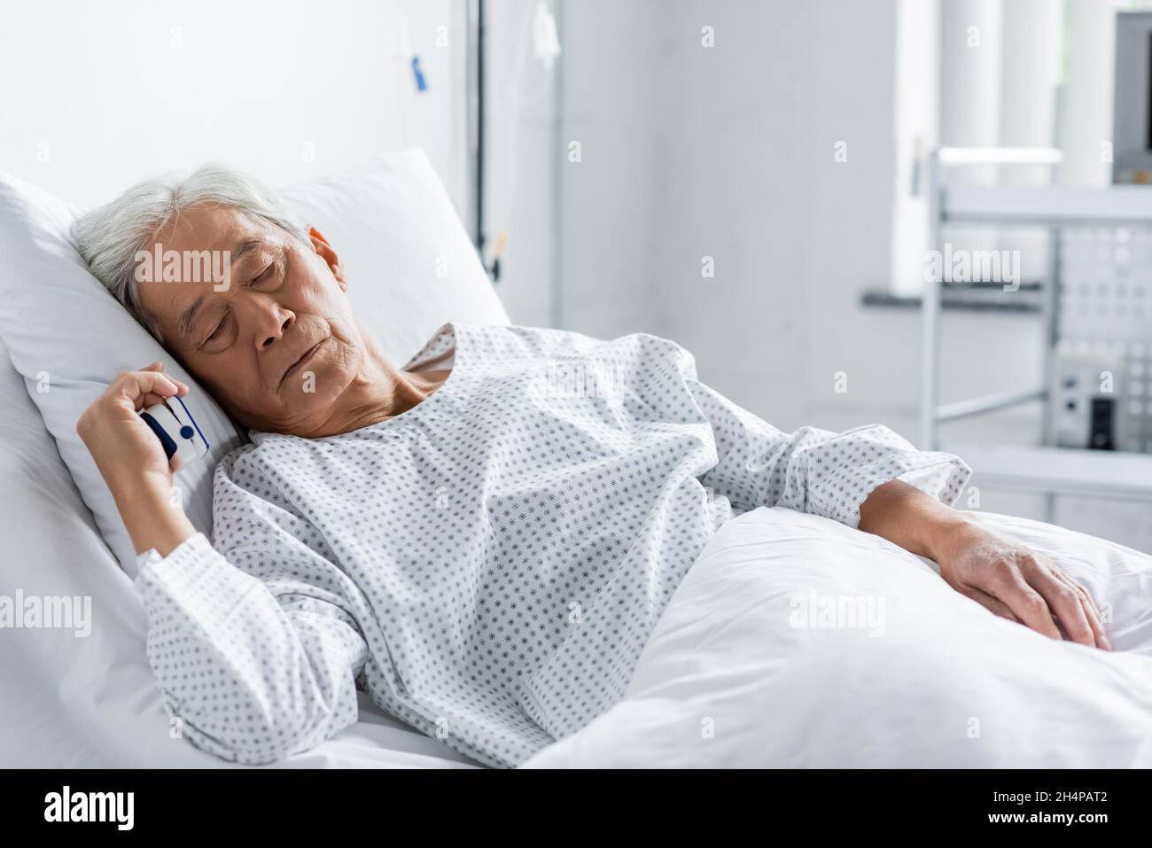 Elderly asian patient with pulse oximeter sleeping on bed in hospital