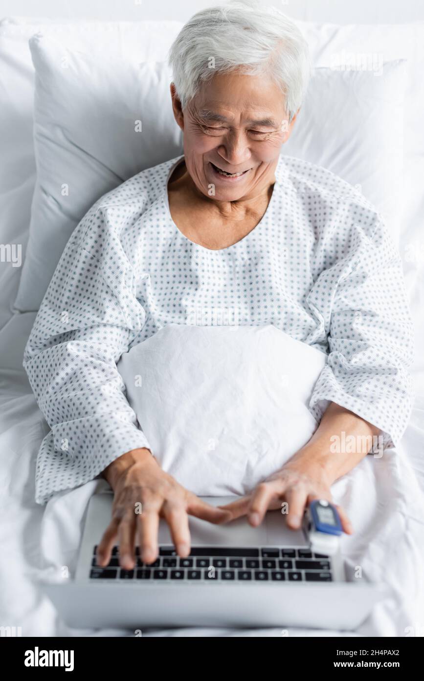 Positive asian patient with pulse oximeter using blurred laptop on bed