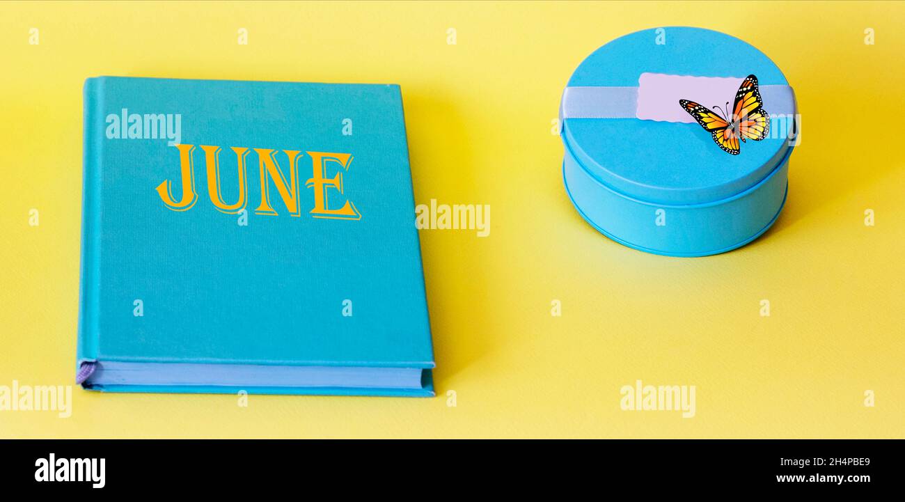 Text June on a turquoise notebook and yellow background, next to a turquoise box and butterfly Stock Photo