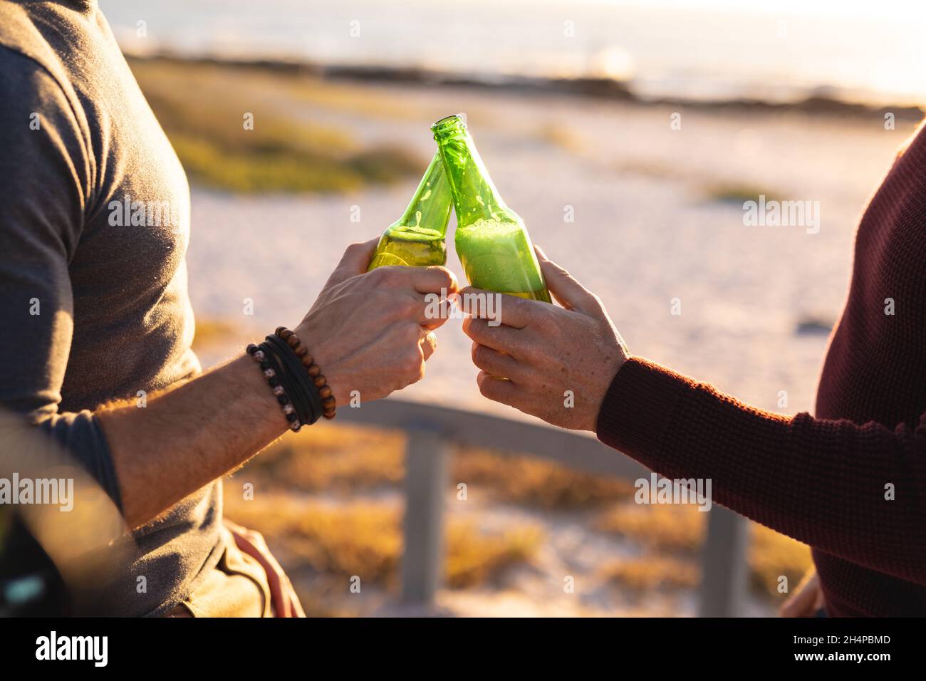 Mid section of caucasian gay male couple making a toast with bottles of beer at seaside Stock Photo