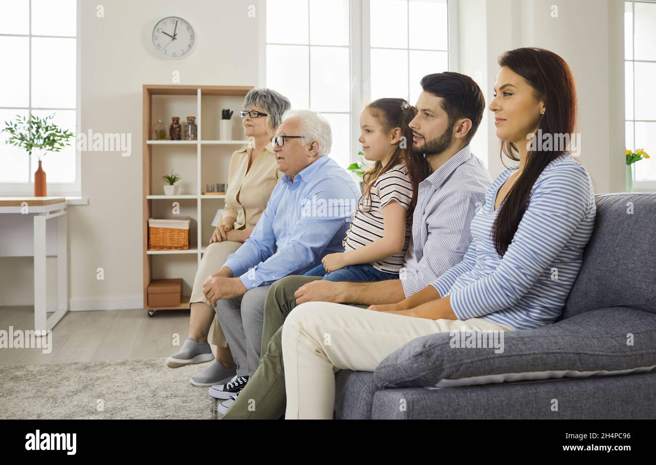 Family of different generations watching a TV talk show together while sitting at home on the couch. Stock Photo