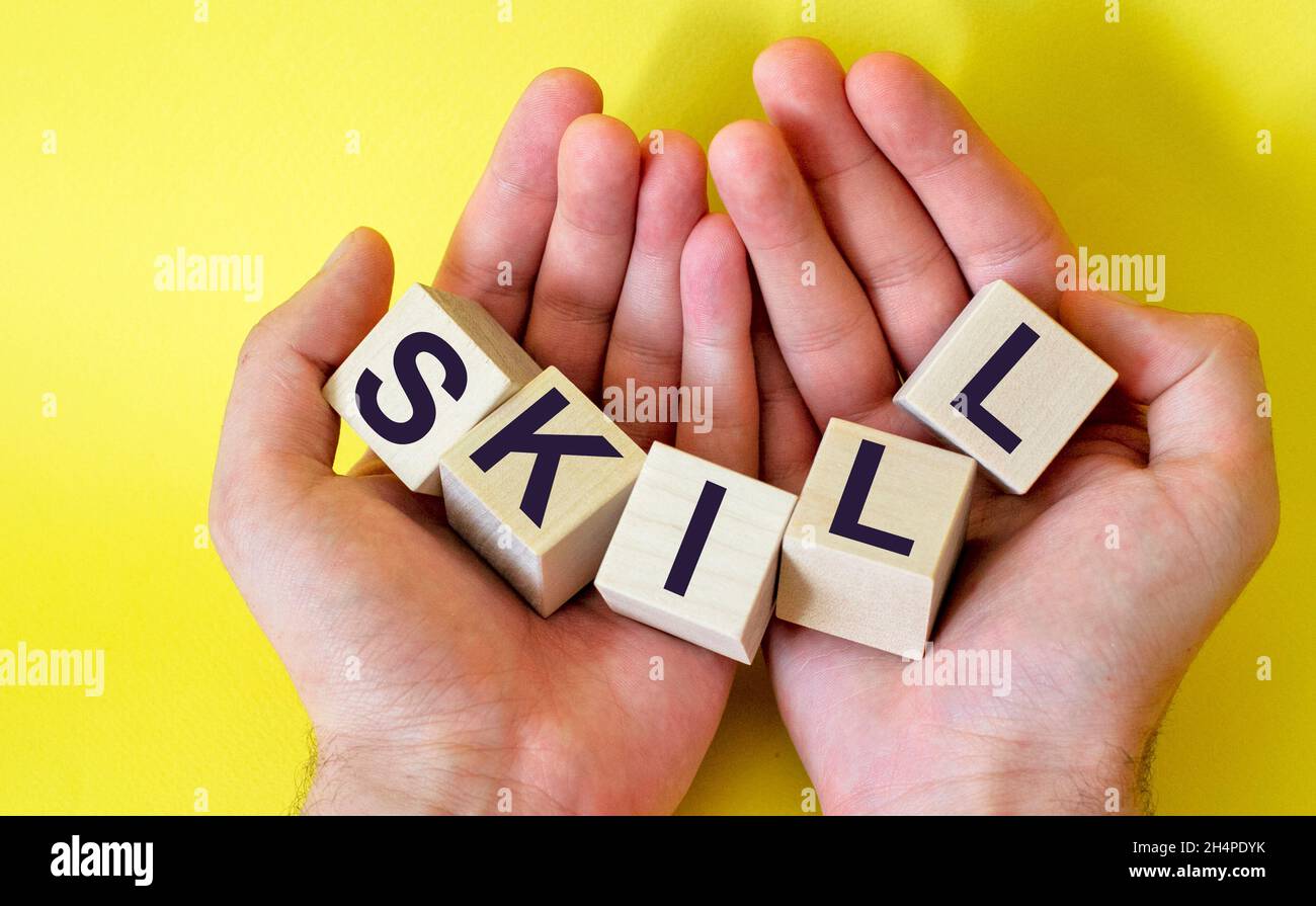 Hands hold wooden blocks with the word Skill, on a yellow background. Stock Photo