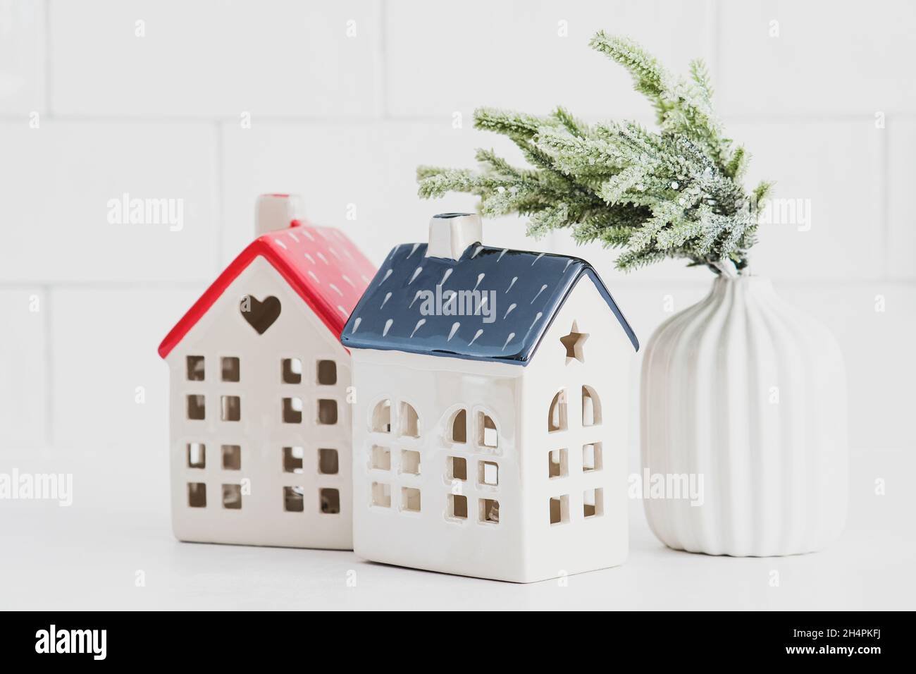 Christmas home decor on white table. Two little ceramic houses and vase with fir branch. Cozy home, hygge, nordic style. Stock Photo