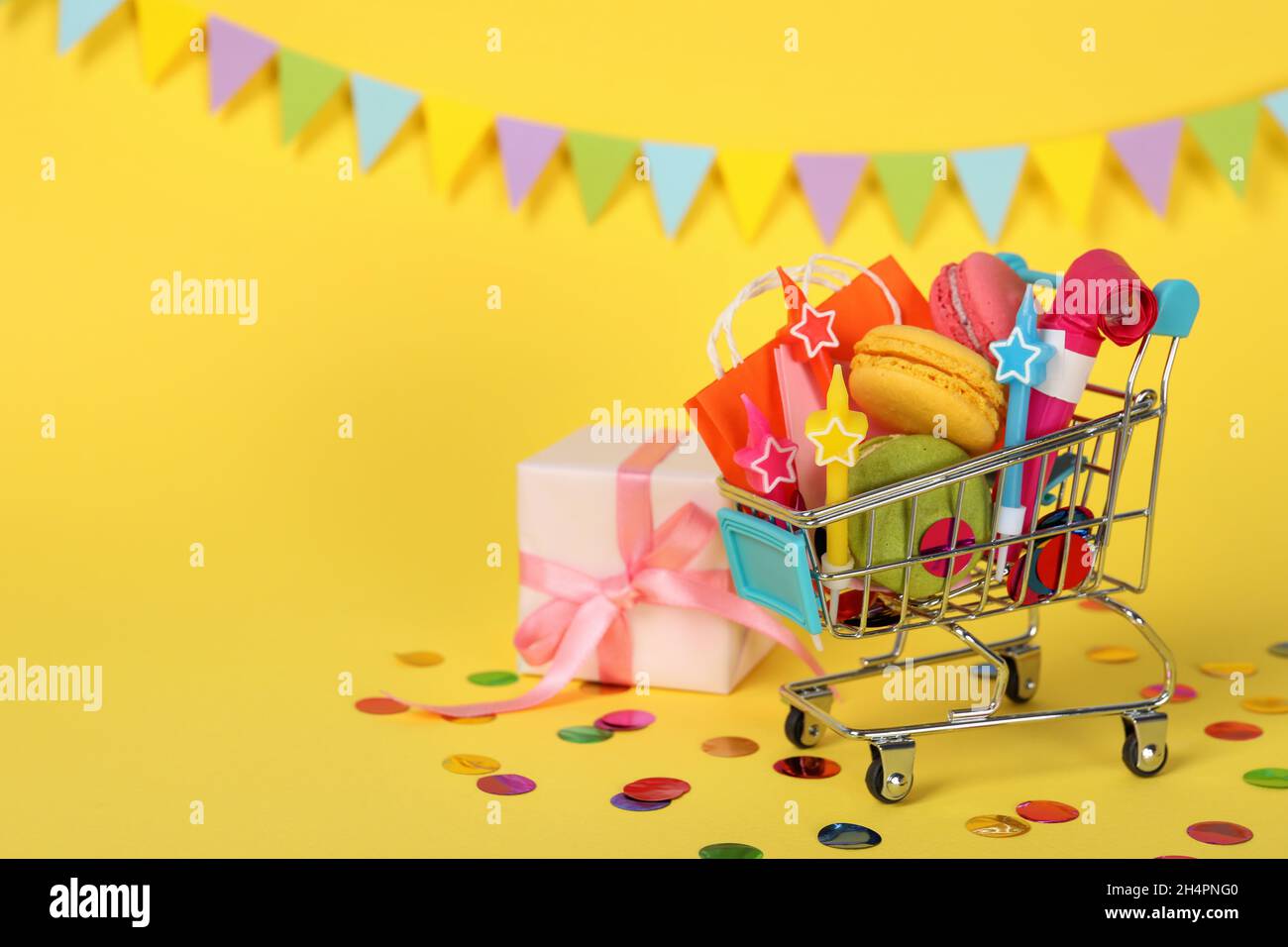 Shop cart with birthday accessories on yellow background, space for