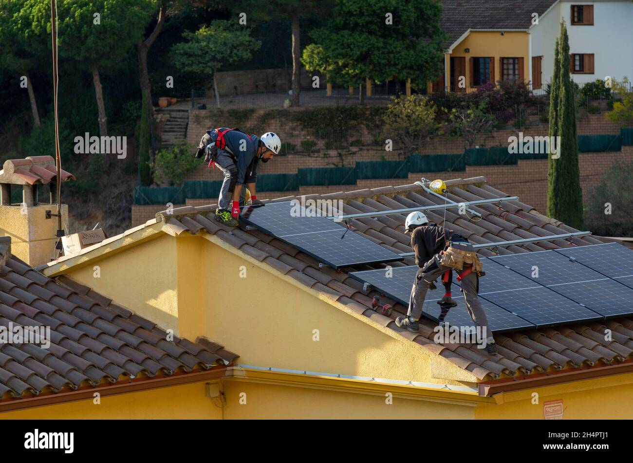 Electrical contract workers for HolaLuz install solar panels on the roof of a residential house during the setup of a subsidised electrical supply system for private homes, north of Barcelona in Carbils, Catalonia, Spain. © Olli Geibel Stock Photo