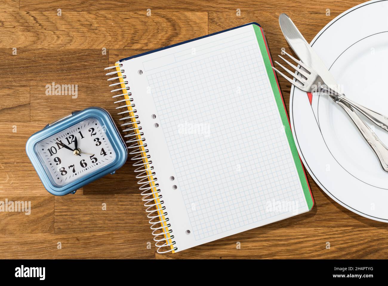Clock, notebook and dish with cutlery on a wooden background. Conceptual image of intermittent fasting, a diet with benefits such as the regenerative Stock Photo