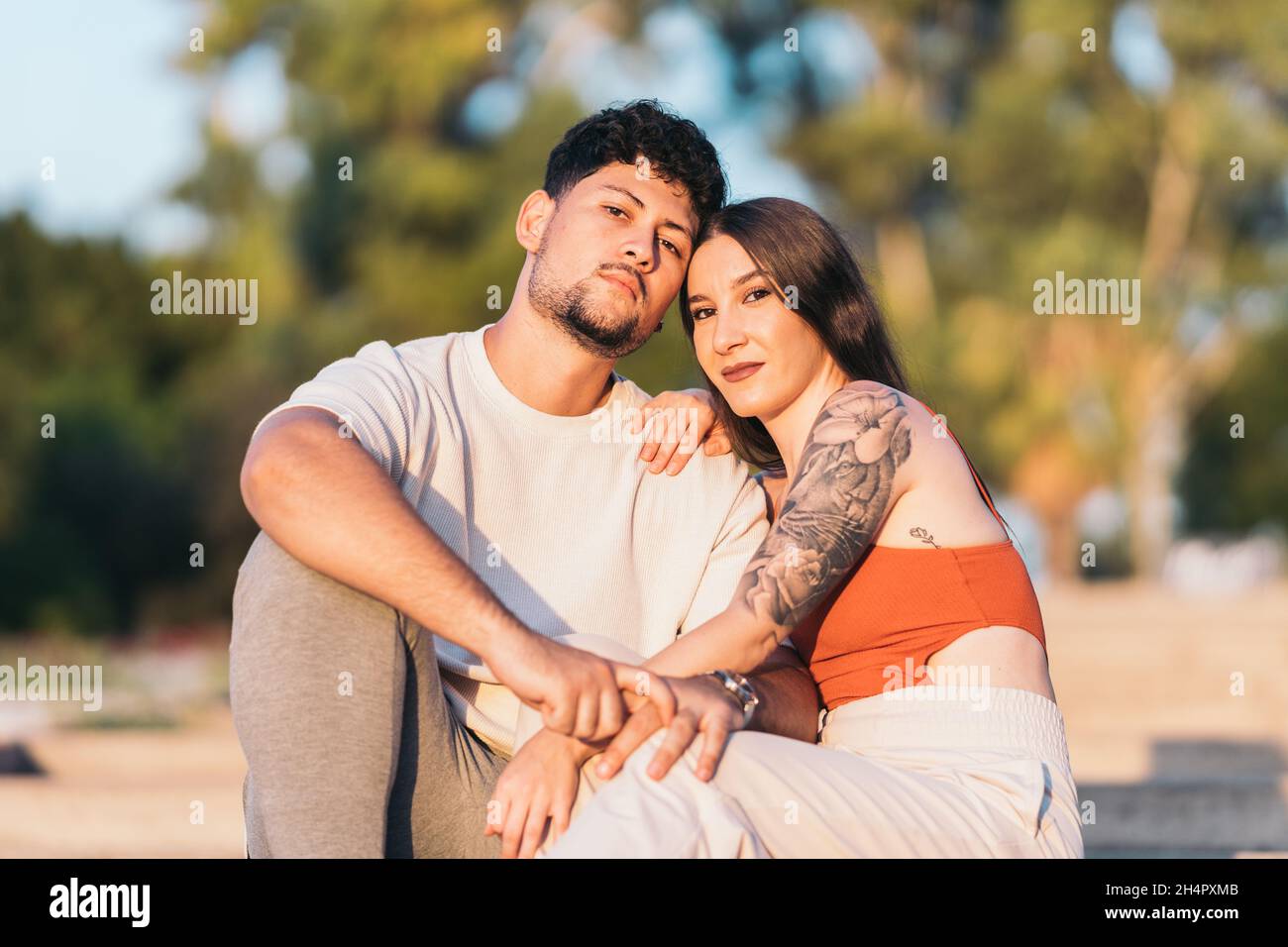 Couple facing the camera while sitting together on a park during sunset Stock Photo
