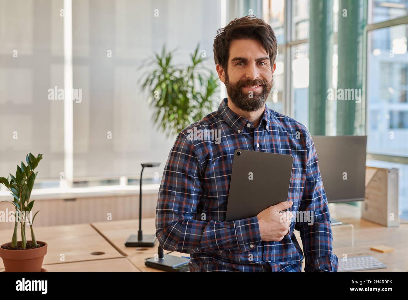 Smiling businessman leaning on his desk holding a digital tablet Stock Photo
