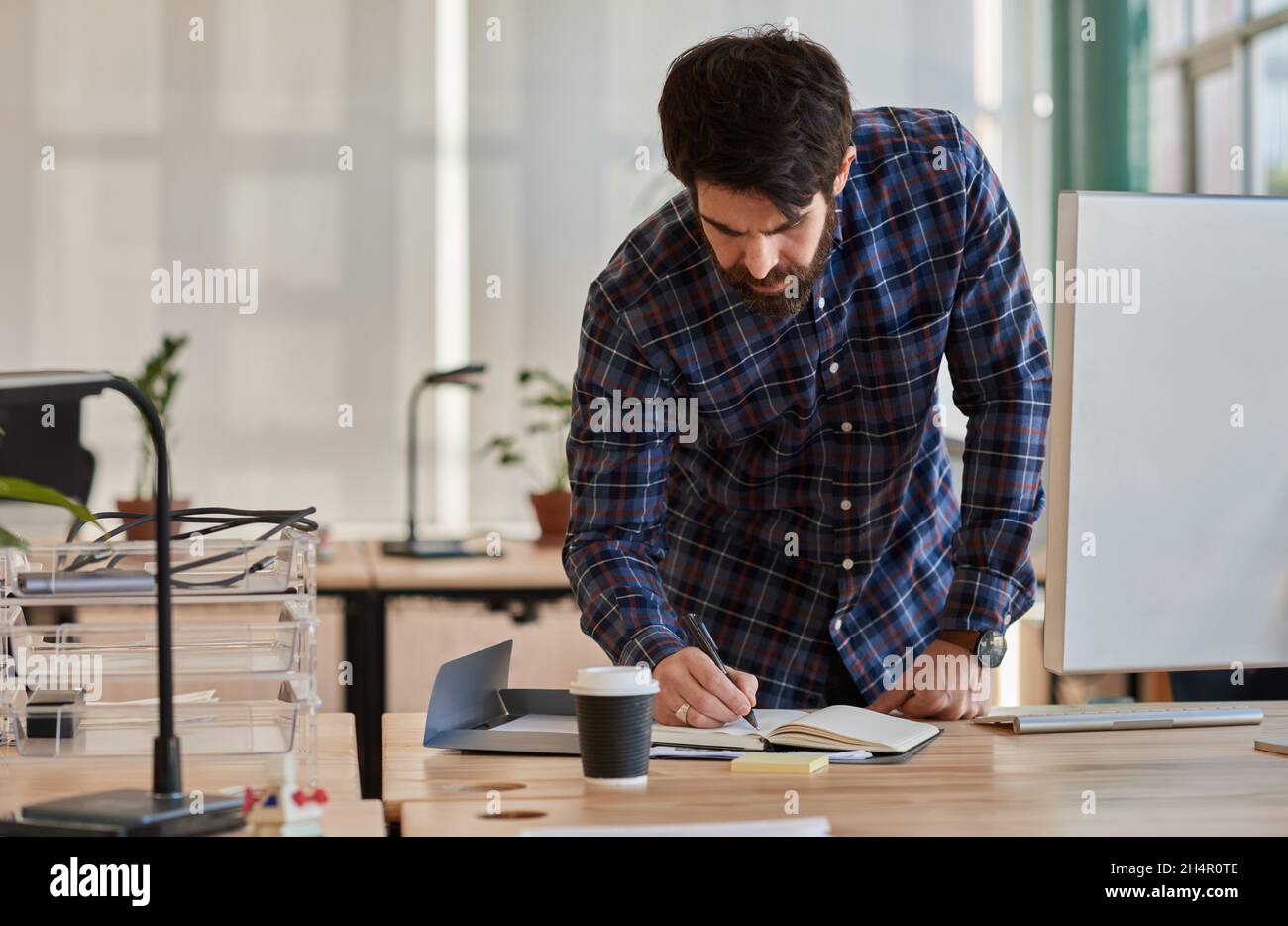 Young businessman leaning over his desk and writing in a notebook Stock Photo