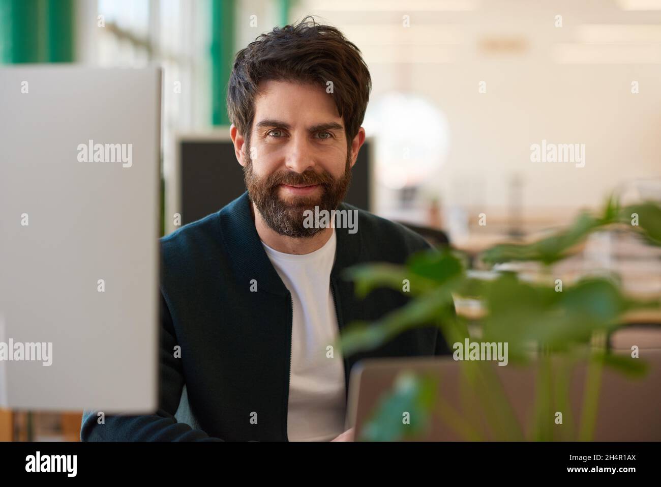 Smiling young businessman working on a laptop at his office desk Stock Photo