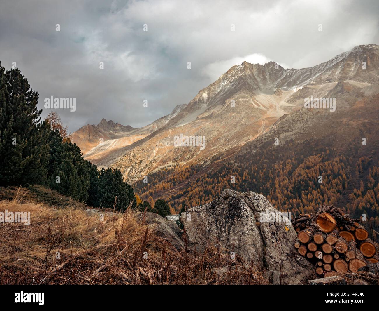Amazing views over an high alpine valley and snow covered mountains. Orange and yellow coloured autumn and fall trees line the valley sides Stock Photo