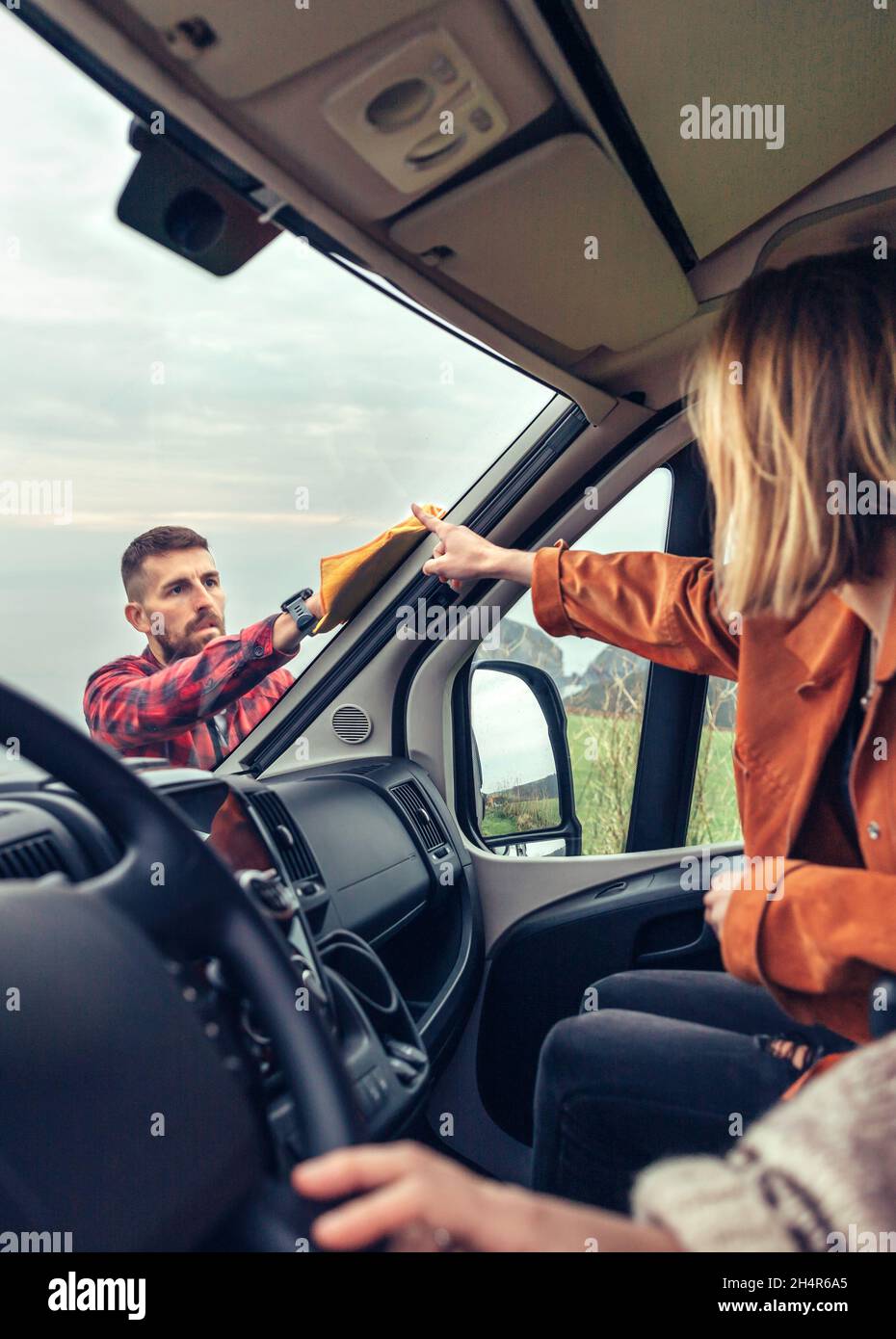 man cleaning motorhome windshield while woman pointing stain Stock